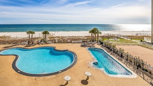 A pool area with two swimming pools, a beach, and a fenced walking path.