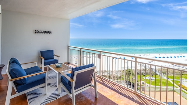 A balcony with a view of the beach, a sign reading "BEACH TOWELS", and a table with chairs.