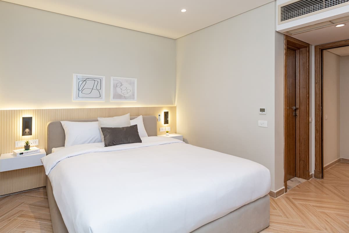 A modern hotel room with a large bed, bedside tables, a wall-mounted light, and two framed pictures.