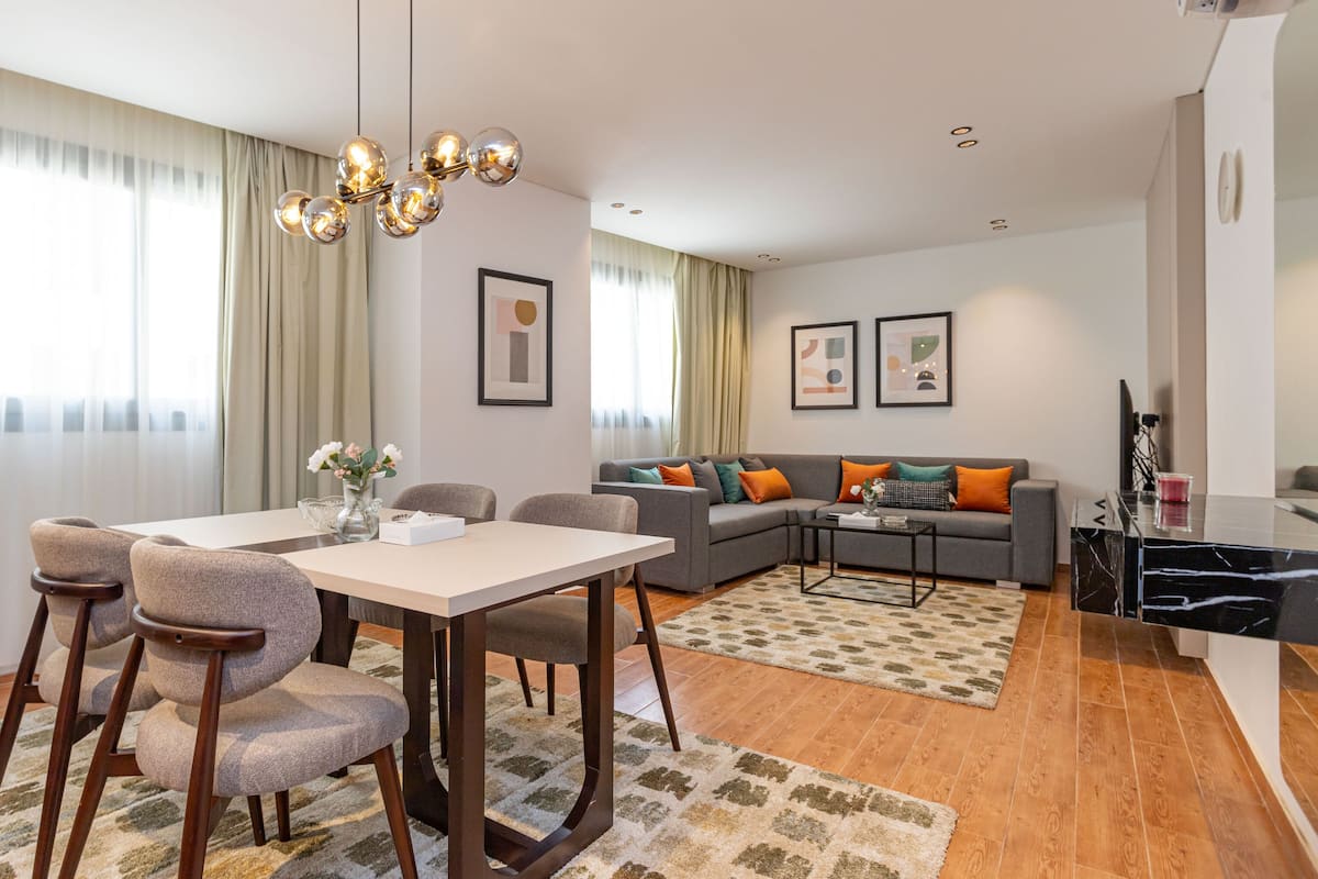 A modern living room with a dining area, featuring a sofa set, a coffee table, and a chandelier.