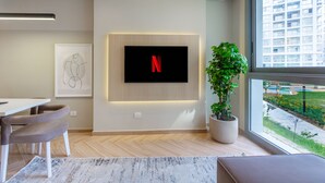 Un salon moderne avec un téléviseur à écran plat fixé au mur, une plante en pot et une vue sur un immeuble par la fenêtre.