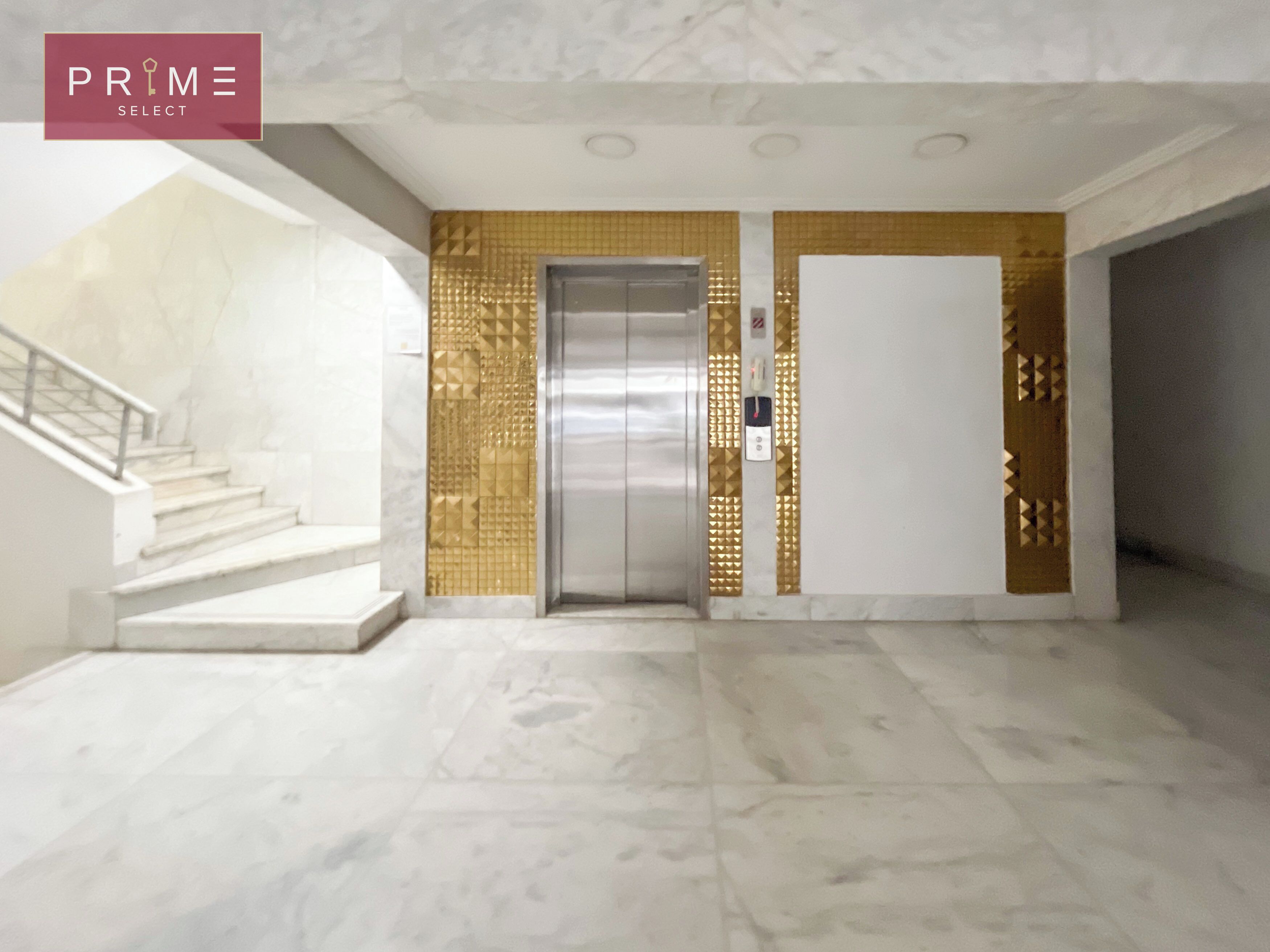 A modern elevator with a metallic finish, a staircase with a glass railing, and a patterned wall design.