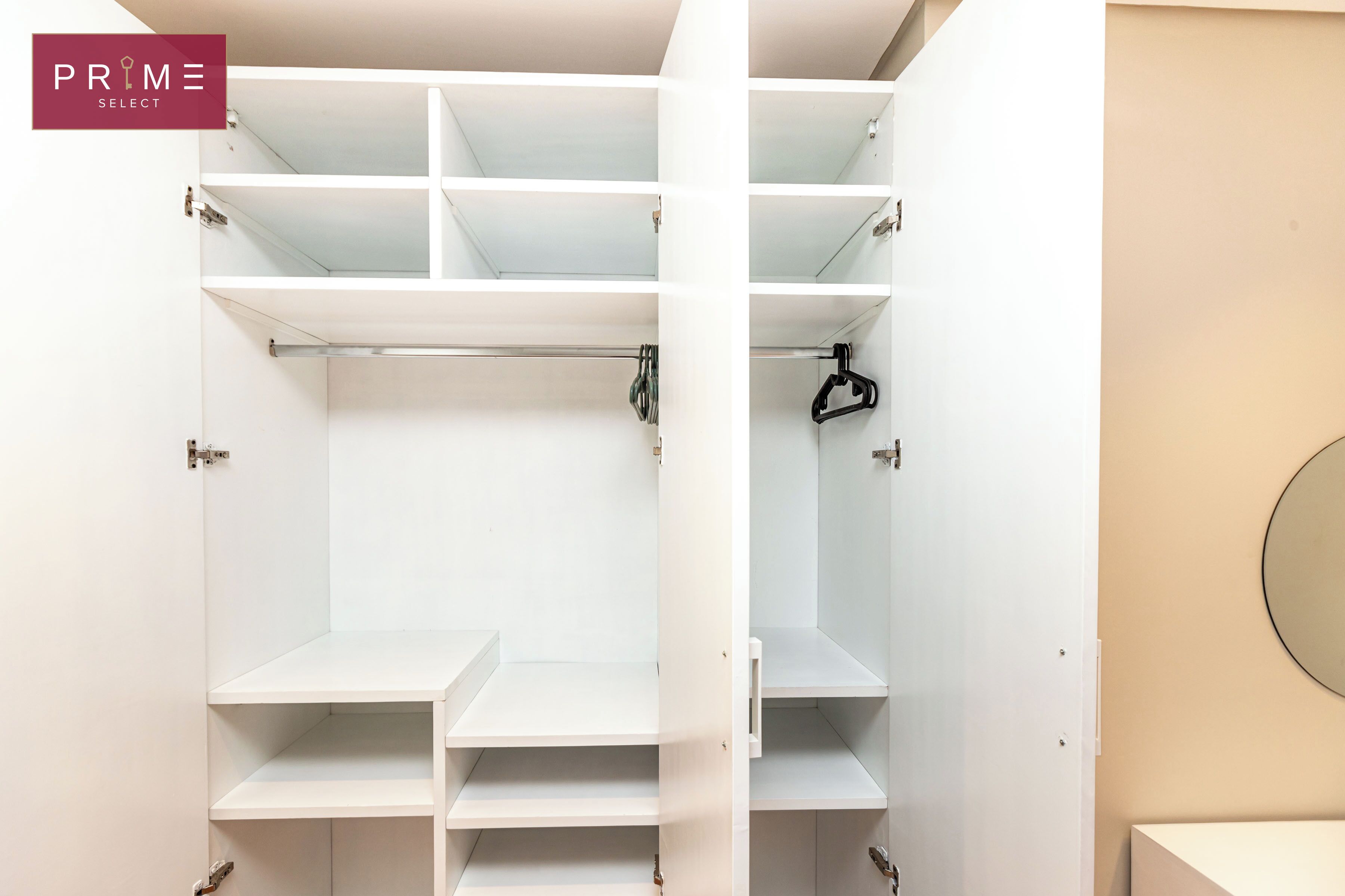 A white closet with multiple shelves and hanging space, featuring a minimalist design and a neutral color palette.
