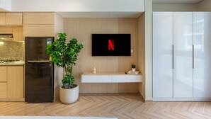 Une cuisine moderne équipée d’une cuisinière intégrée, d’un réfrigérateur, d’une plante en pot, d’un téléviseur fixé au mur affichant le logo de Netflix et d’une armoire blanche.