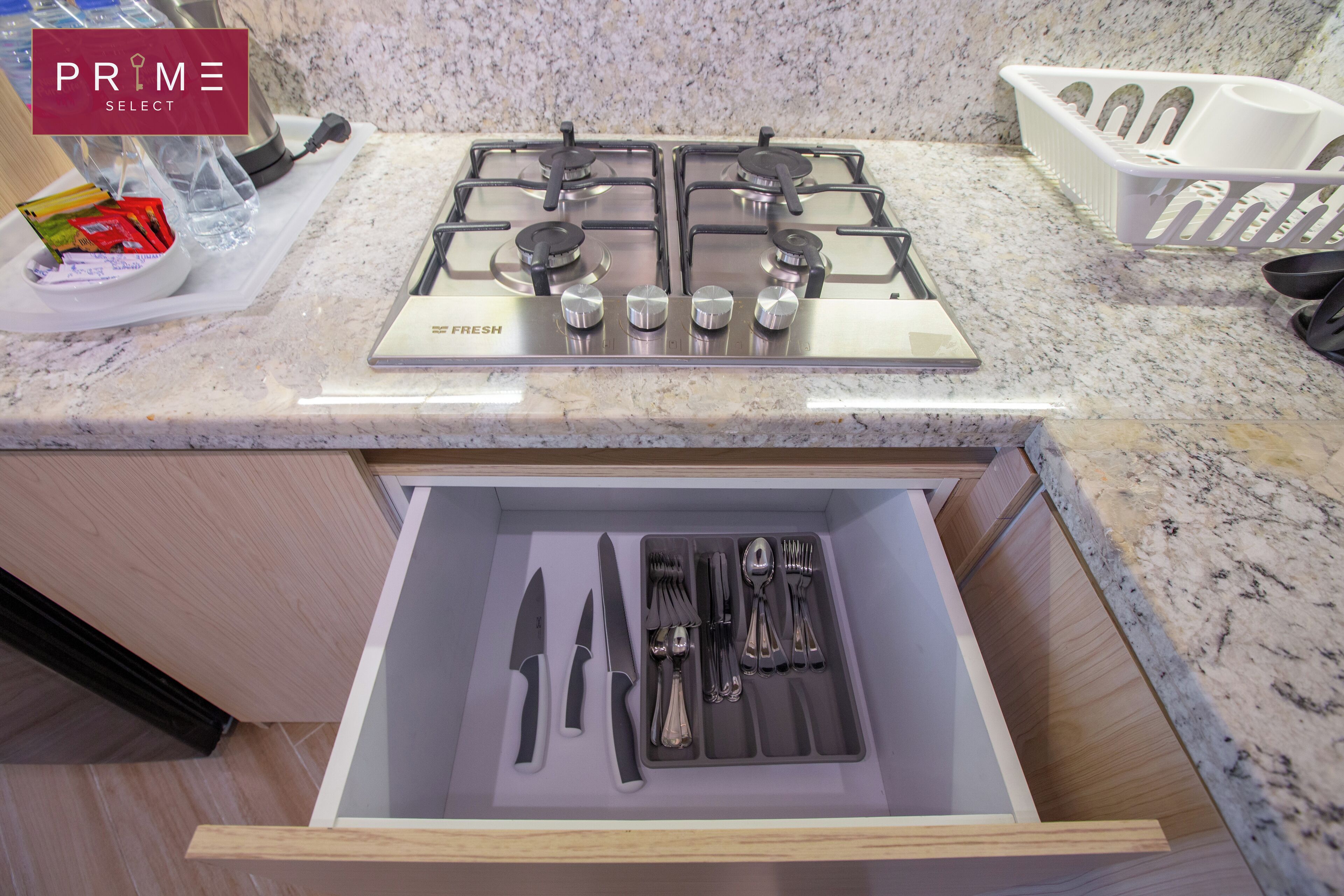 A kitchen with a gas stove, a drawer with cutlery, and a granite countertop.