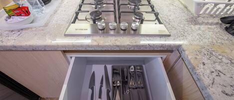 A kitchen with a gas stove, a drawer with cutlery, and a granite countertop.