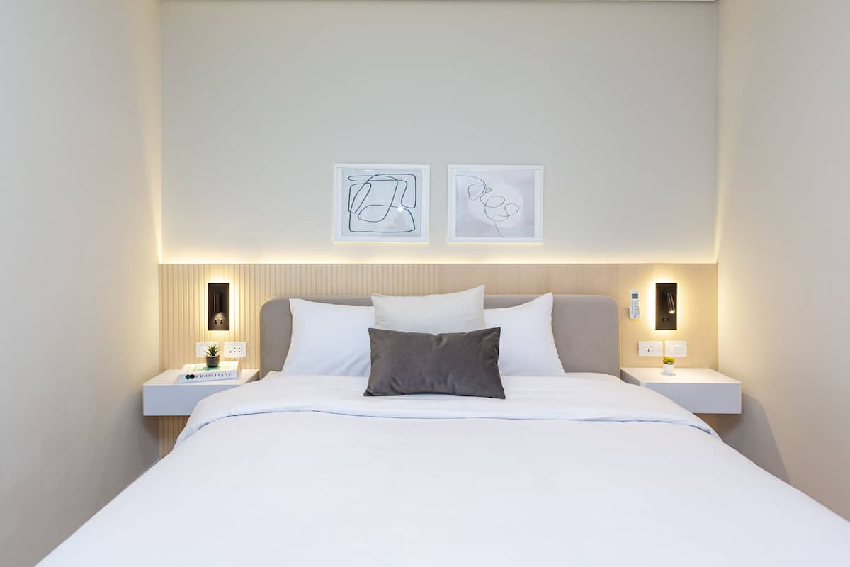 A neatly made bed with white linens, two bedside tables with lamps, and two framed artworks on the wall.