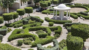 Un jardin aménagé avec un kiosque central, des haies taillées et un chemin pavé.