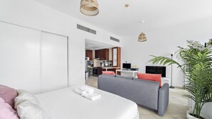 Une chambre d’hôtel moderne avec un lit, un canapé gris, un petit bureau, une télévision et une plante en pot.