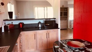 A kitchen with a black countertop, wooden cabinets, a microwave, a kettle, and a toaster. - Maison Familial, Piscine Privée, à 5mins des Plages de Santa-guilia, Palombaggia (Porto-Vecchio)