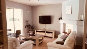A modern living room with a flat-screen TV, a coffee table, two white sofas, and a dining area with a glass table. - Maison Familial, Piscine Privée, à 5mins des Plages de Santa-guilia, Palombaggia (Porto-Vecchio)