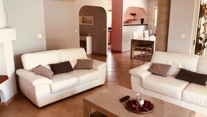 A modern living room with two white sofas, a wooden coffee table, and a dining area in the background. - Maison Familial, Piscine Privée, à 5mins des Plages de Santa-guilia, Palombaggia (Porto-Vecchio)