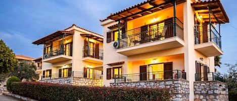 A two-story building with balconies, stone walls, and a well-maintained garden.