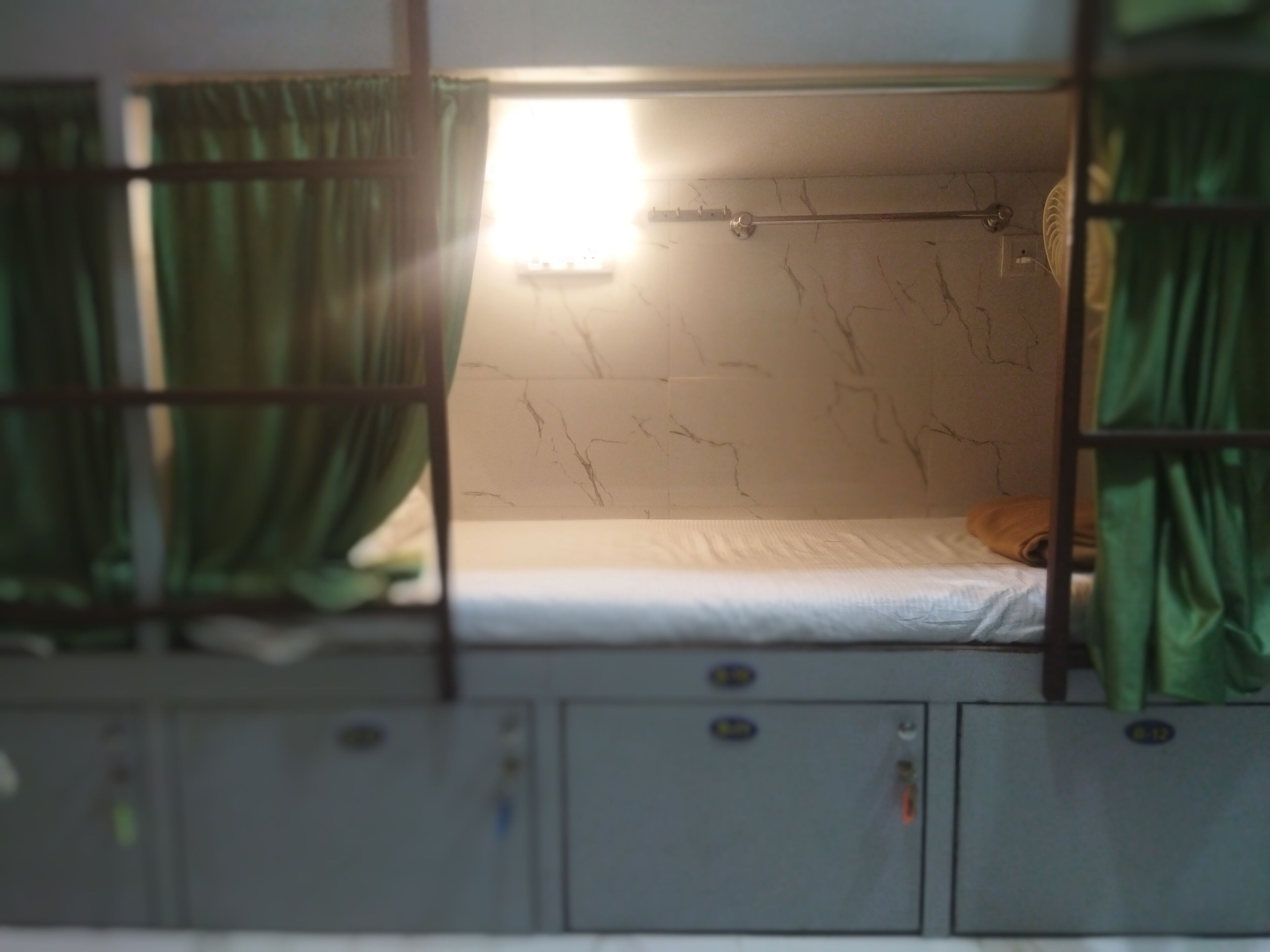 Un lit superposé avec un matelas, une fenêtre avec des rideaux et un mur présentant des fissures apparentes.
