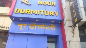Um edifício azul e vermelho com uma placa que diz "NOOR DORMITORY" em inglês e hindi.