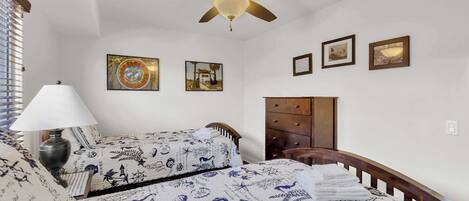 Een slaapkamer met twee bedden, een plafondventilator, een lamp en een dressoir.