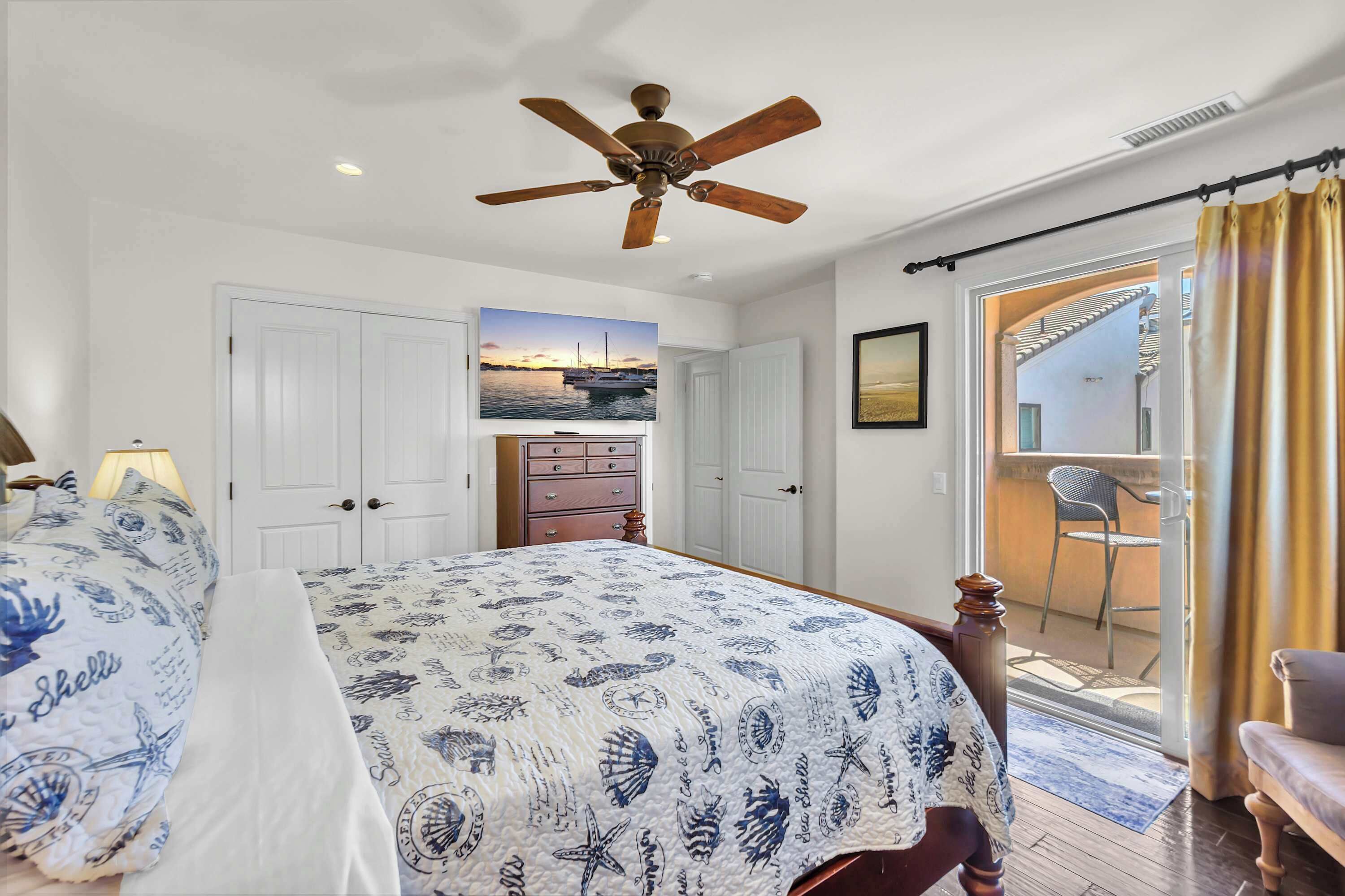 A bedroom with a bed, a ceiling fan, a door, a window, and a view of the outside.