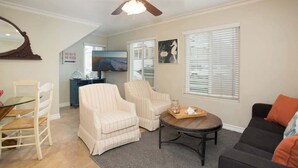 A living room with a ceiling fan, a dining table with chairs, a sofa, and a coffee table. There are two armchairs, a TV, and a window with blinds. - 114 31st A | Rare 1 bdr On Peninsula 3 Houses To Sand (Newport Beach)