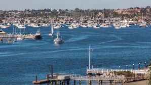 A marina with numerous boats docked, a pier with a railing, and a residential area in the background. - 114 31st A | Rare 1 bdr On Peninsula 3 Houses To Sand (Newport Beach)