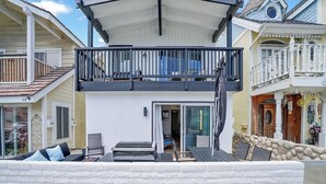 A two-story house with a balcony, a white exterior, and a stone wall in front. - 117 31st St A | Stylish Renovation w/ Large Patio Steps To Sand (Newport Beach)