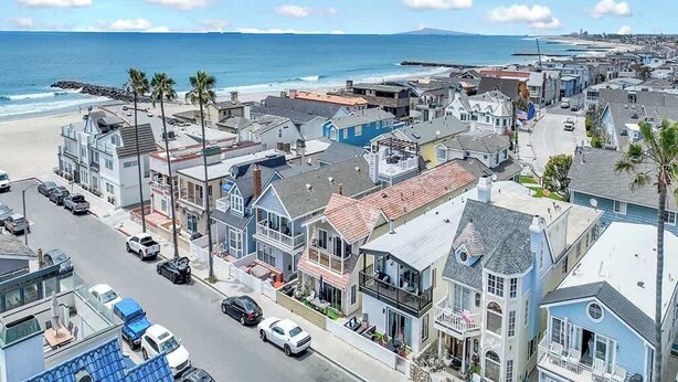 A coastal town with a mix of residential and commercial buildings, a clear view of the ocean, and a road with parked cars. - 117 31st St A | Stylish Renovation w/ Large Patio Steps To Sand (Newport Beach)