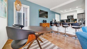 A modern living room with a round table, four black chairs, a blue sofa, and a kitchen in the background. - 117 31st St A | Stylish Renovation w/ Large Patio Steps To Sand (Newport Beach)