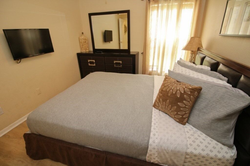 A bedroom with a bed, a dresser, a television, and a window with curtains.