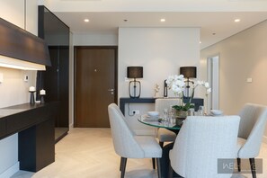 A modern dining area with a glass table, two grey upholstered chairs, a dark wooden cabinet, and a wall-mounted lamp. - WelHome - Luxurious 2BR Apt in Forte T1 Downtown (Dubai)