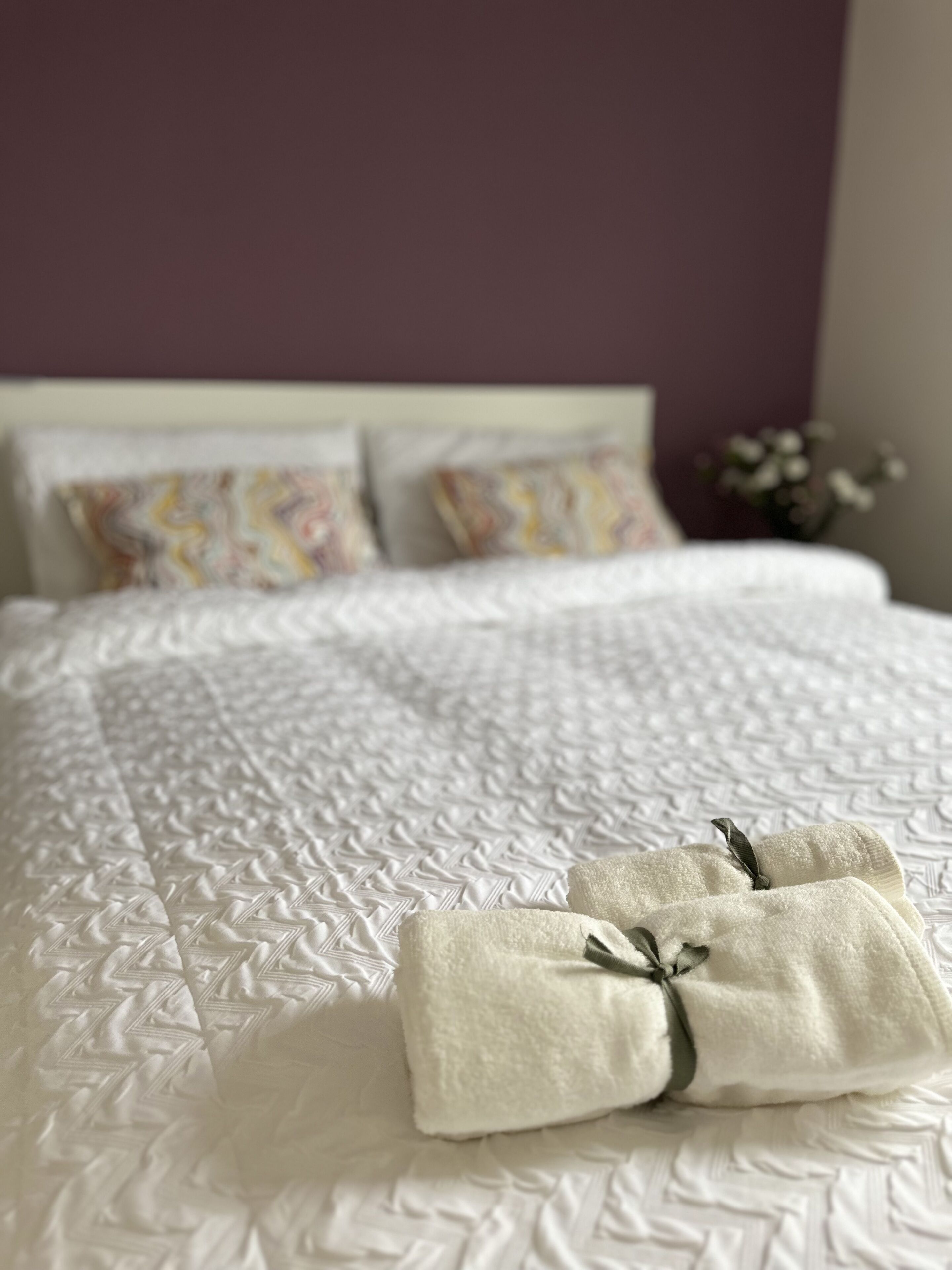 A neatly made bed with a white quilt and two folded towels with a ribbon.