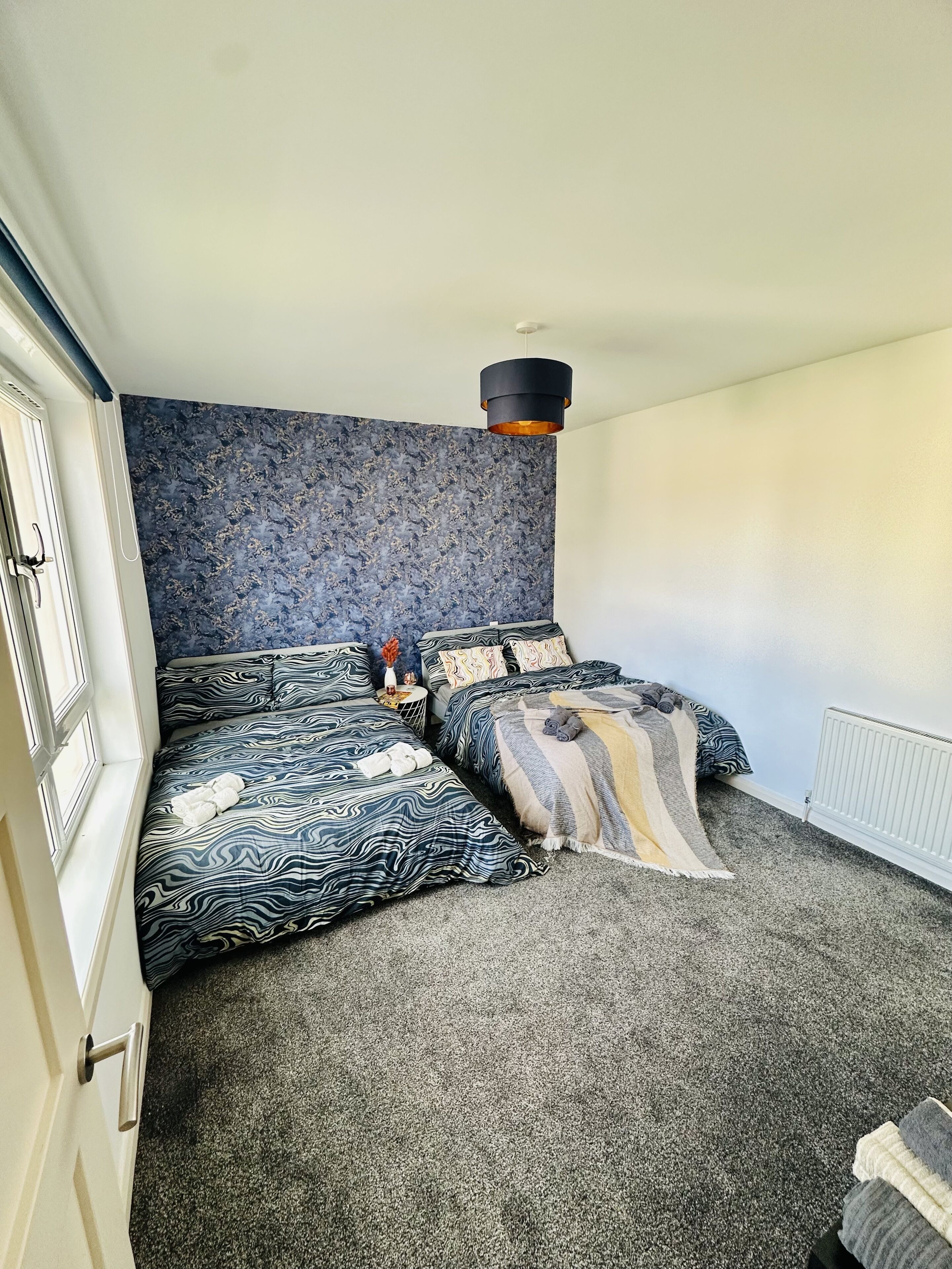 A bedroom with a large bed, a side table, and a patterned wall.
