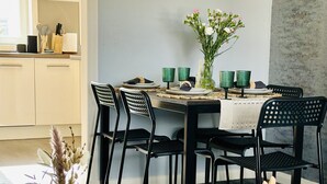 Un comedor con una mesa redonda, sillas negras, un jarrón con flores secas y una mano de madera.