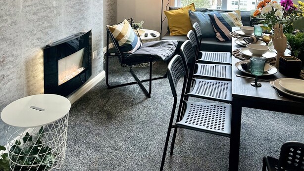 Una sala de estar moderna con chimenea, un televisor de pantalla plana montado en una pared con textura, un comedor con mesa para cuatro personas y un gran ventanal con vistas al exterior.