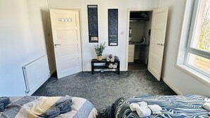 Un dormitorio con dos camas, una lámpara en el techo, un radiador, una mesita con una planta y un armario.