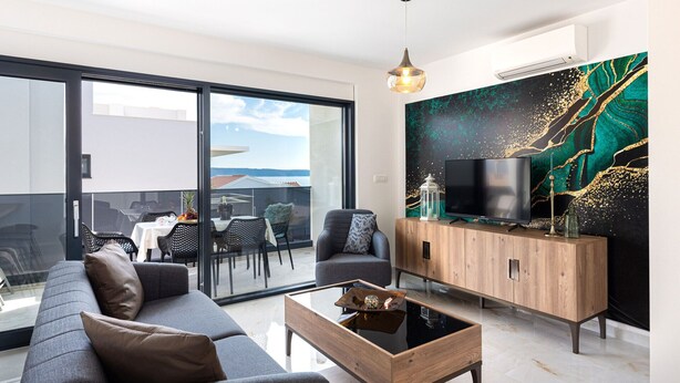 A modern living room with a sofa, coffee table, and TV, featuring a large window and a decorative wall. - Apartment Simo- stylish two bedroom apartment (Okrug Gornji)
