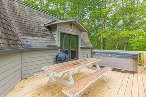 Una terraza de madera con mesas de picnic, un jacuzzi y una zona cubierta con puerta.