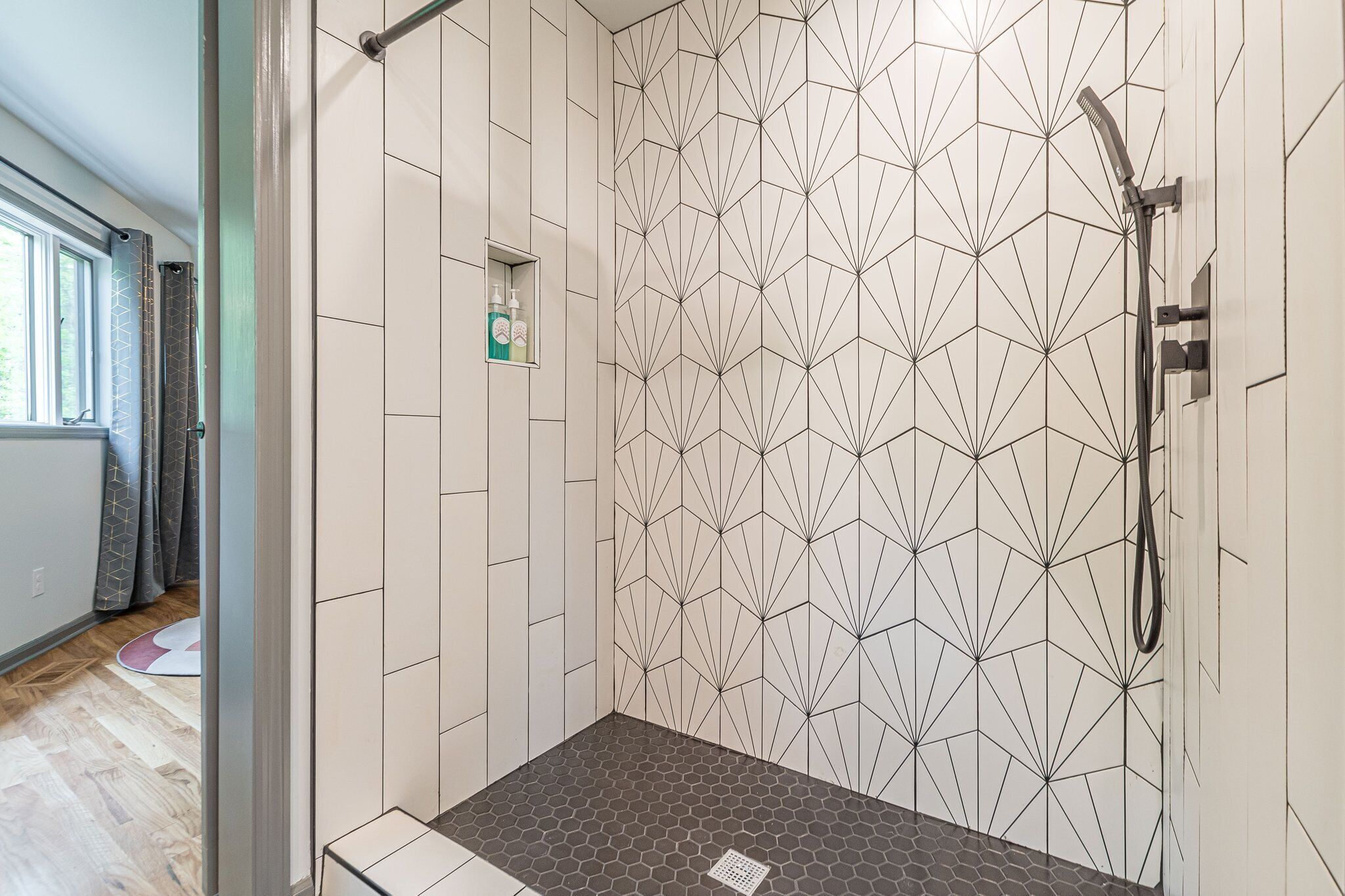 Une douche avec un carrelage aux motifs géométriques, une douchette à main et une petite étagère pour les articles de toilette.