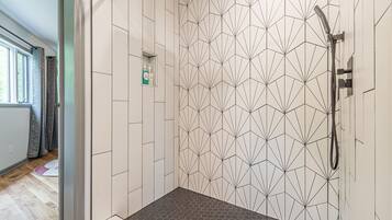 Une douche avec un carrelage aux motifs géométriques, une douchette à main et une petite étagère pour les articles de toilette.