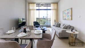 A modern living room with a dining area, a sofa, and a TV. - WelHome - Prime 1BR Apartment at Oia Residence (Dubai)