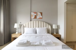 Un lit bien fait, avec du linge de lit blanc, deux tables de chevet avec des lampes et un mur orné de deux œuvres d’art encadrées.