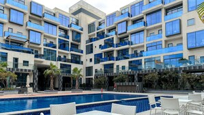 A modern hotel with a central pool, outdoor seating, and a multi-story building with balconies. - WelHome - Prime 1BR Apartment at Oia Residence (Dubai)