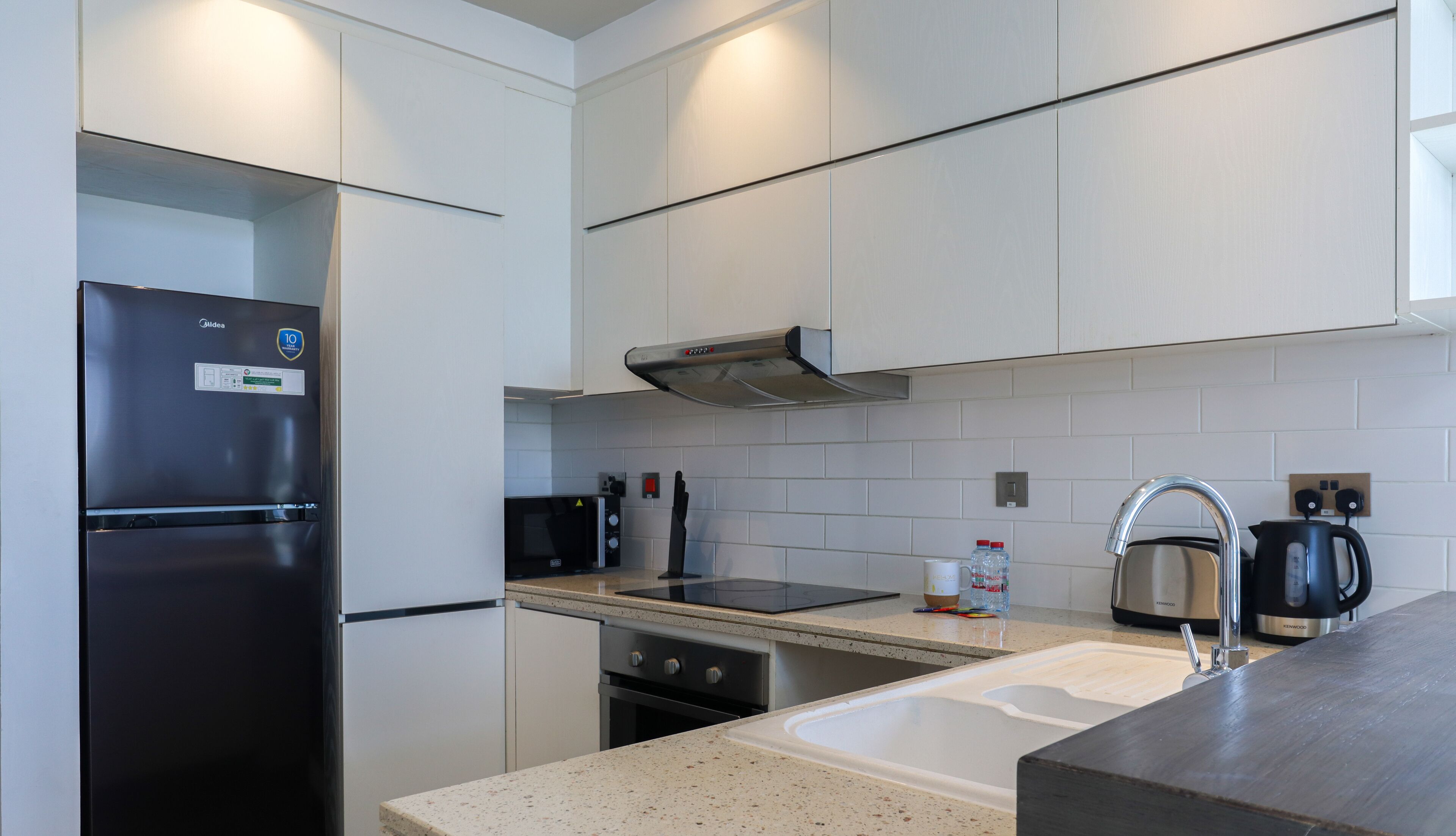 A modern kitchen with a stainless steel refrigerator, a built-in oven, a microwave, a kettle, and a sink.