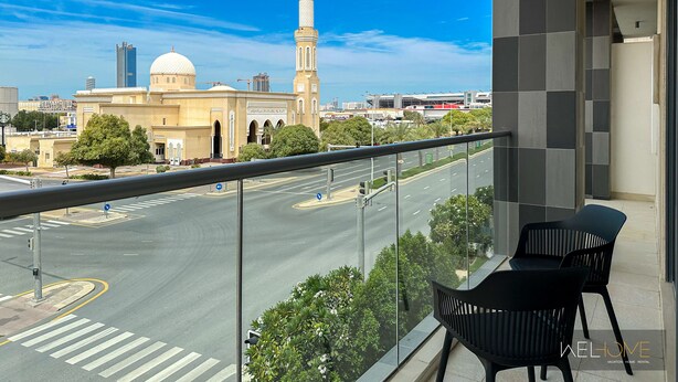 A balcony with a view of a mosque, a road, and a modern building. - WelHome - Prime 1BR Apartment at Oia Residence (Dubai)