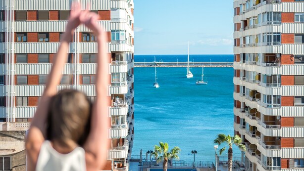 A person standing on a balcony overlooking a marina with sailboats, with modern buildings and palm trees in the background. - 150m from the beach, 3-bedroom apartment with nice living room and office area (Torrevieja)