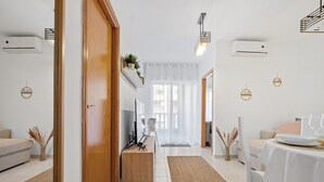 A modern living room with a wooden door, a sofa, a coffee table, and a dining area with a table set for two. - 150m from the beach, 3-bedroom apartment with nice living room and office area (Torrevieja)