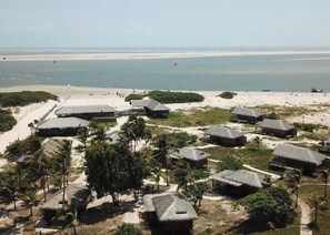 Um resort costeiro com palmeiras, cabanas de palha e vista para a praia.