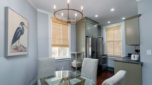 A modern kitchen with a glass dining table, grey chairs, a chandelier, and a refrigerator.