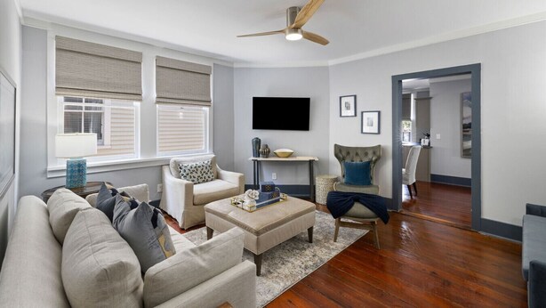 A living room with a sofa, armchair, ottoman, and a ceiling fan.