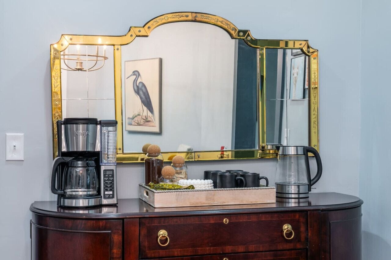 Un aparador de madera oscura con un espejo, una cafetera, un hervidor y una bandeja con objetos decorativos.