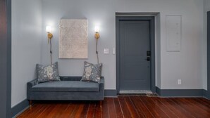 A room with a grey sofa, two wall-mounted lamps, a patterned wall hanging, and a grey door.