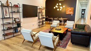 Ein modernes Wohnzimmer mit Flachbildfernseher, Couchtisch aus Holz, weißen und schwarzen Sofas sowie einem Essbereich mit einer Chandelier.